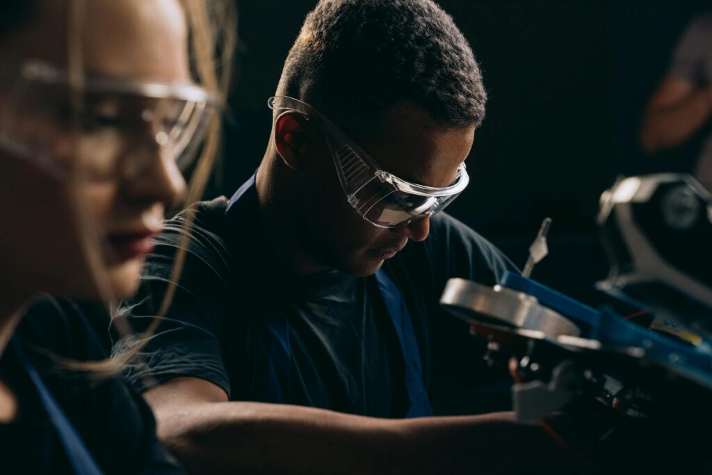 Students focused on robotics, wearing protective goggles, symbolizing teamwork and education in technology.